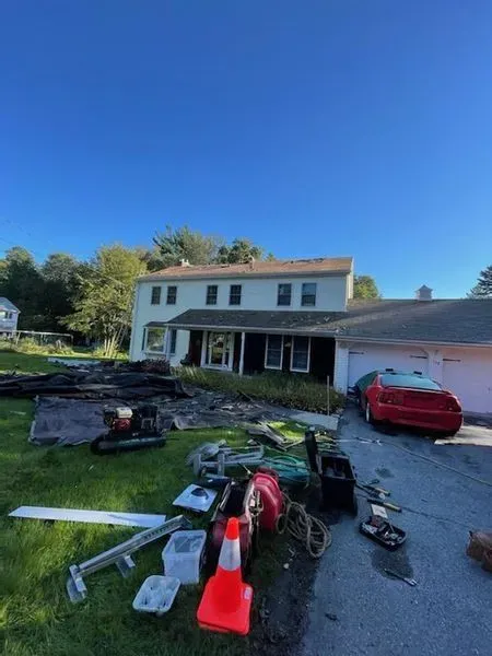 House with yard full of debris and car in driveway under clear, blue sky.