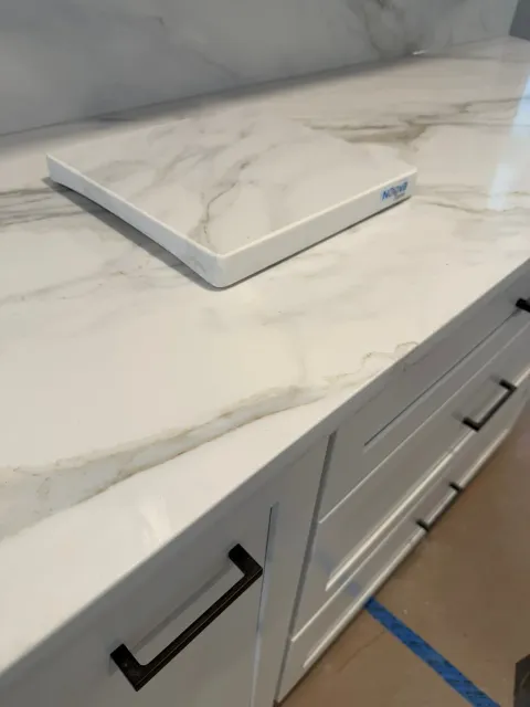 White marble cutting board on a light marble kitchen counter with white cabinets below