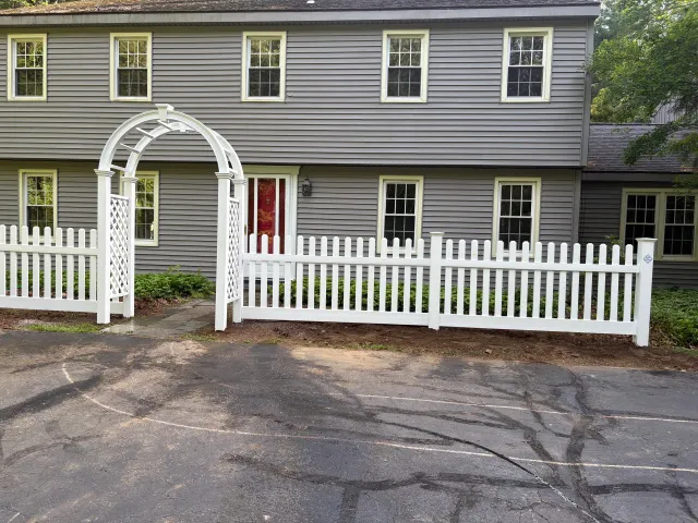 A white picket fence is in front of a gray house