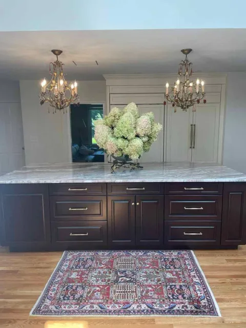 Kitchen island with dark cabinetry, marble countertop, and chandeliers. Hydrangeas sit on the island, and a rug on the hardwood floor.