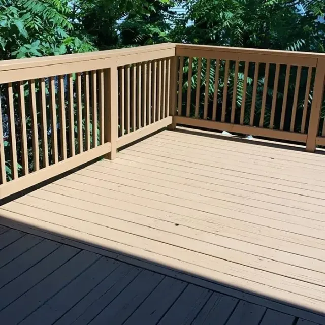 Wooden deck with light tan boards and railing, bordered by trees and greenery