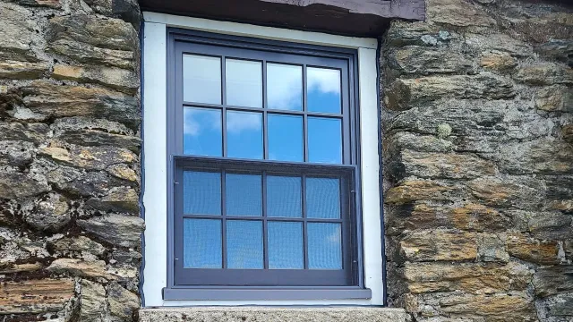 Blue-framed window set in a rough stone wall, with reflected sky and closed curtains behind the glass.