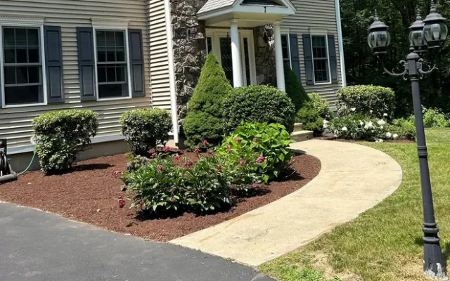 Two-story house with tan siding, backyard with green lawn, patio furniture, and landscaping.