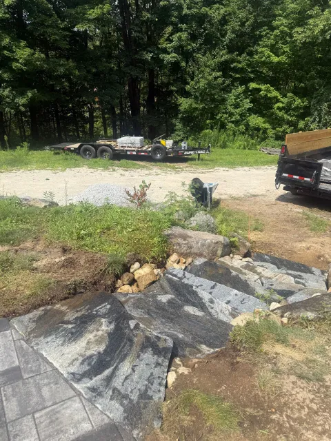 Rock-bordered gravel driveway beside a black car, with a stone path and trees in the background
