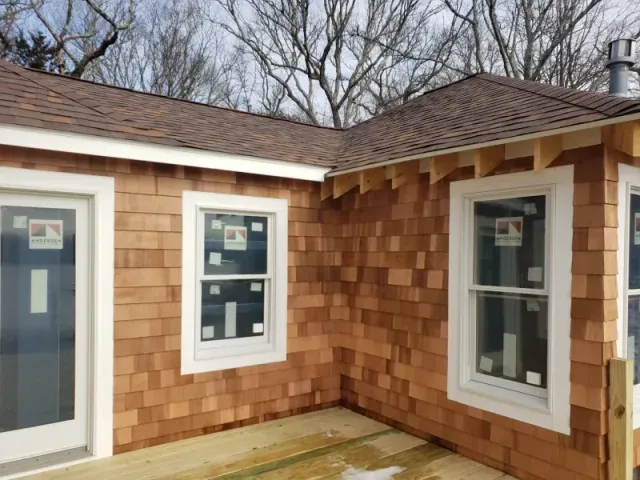 Exterior of house under construction with brown shingle siding, white windows, and wooden deck.