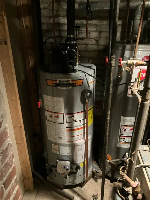 Tall silver water heater in a narrow utility closet with pipes and valves around it