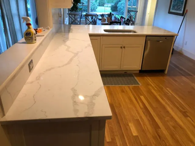 A kitchen with white cabinets , a sink , and a wooden floor.