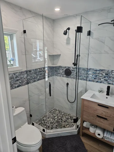 Modern bathroom with a glass-enclosed shower, wood vanity, and mosaic tile accents.