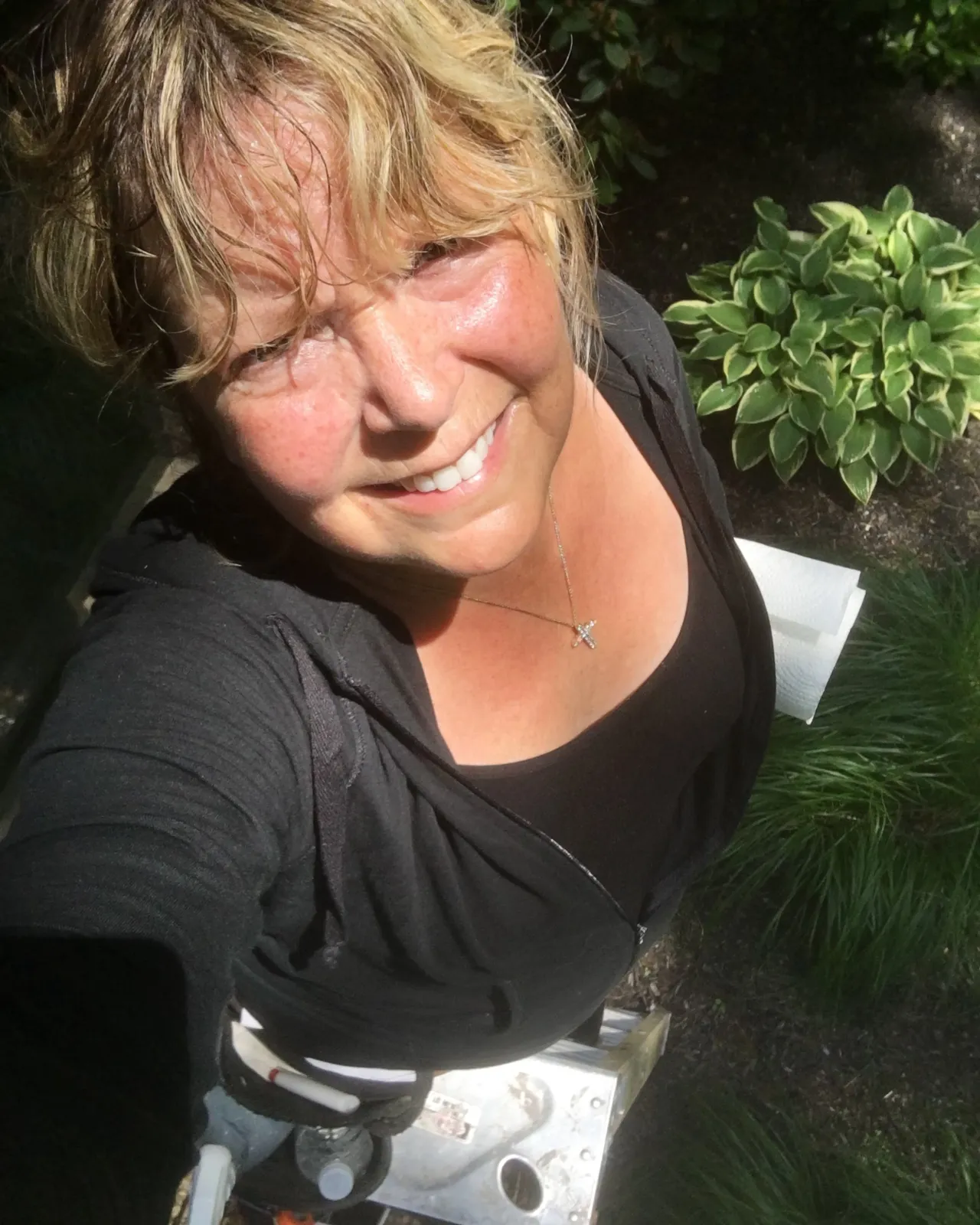Person smiling outdoors with green plants in the background.