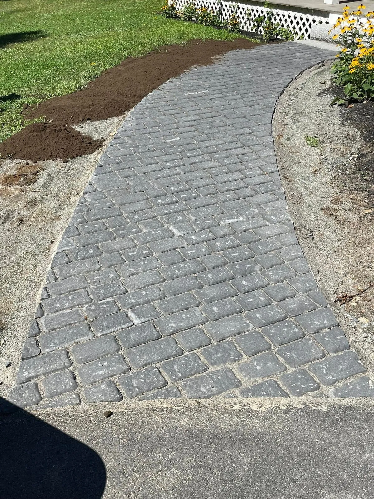 Brick pathway curves through a green yard. Brown dirt and gravel border the path.