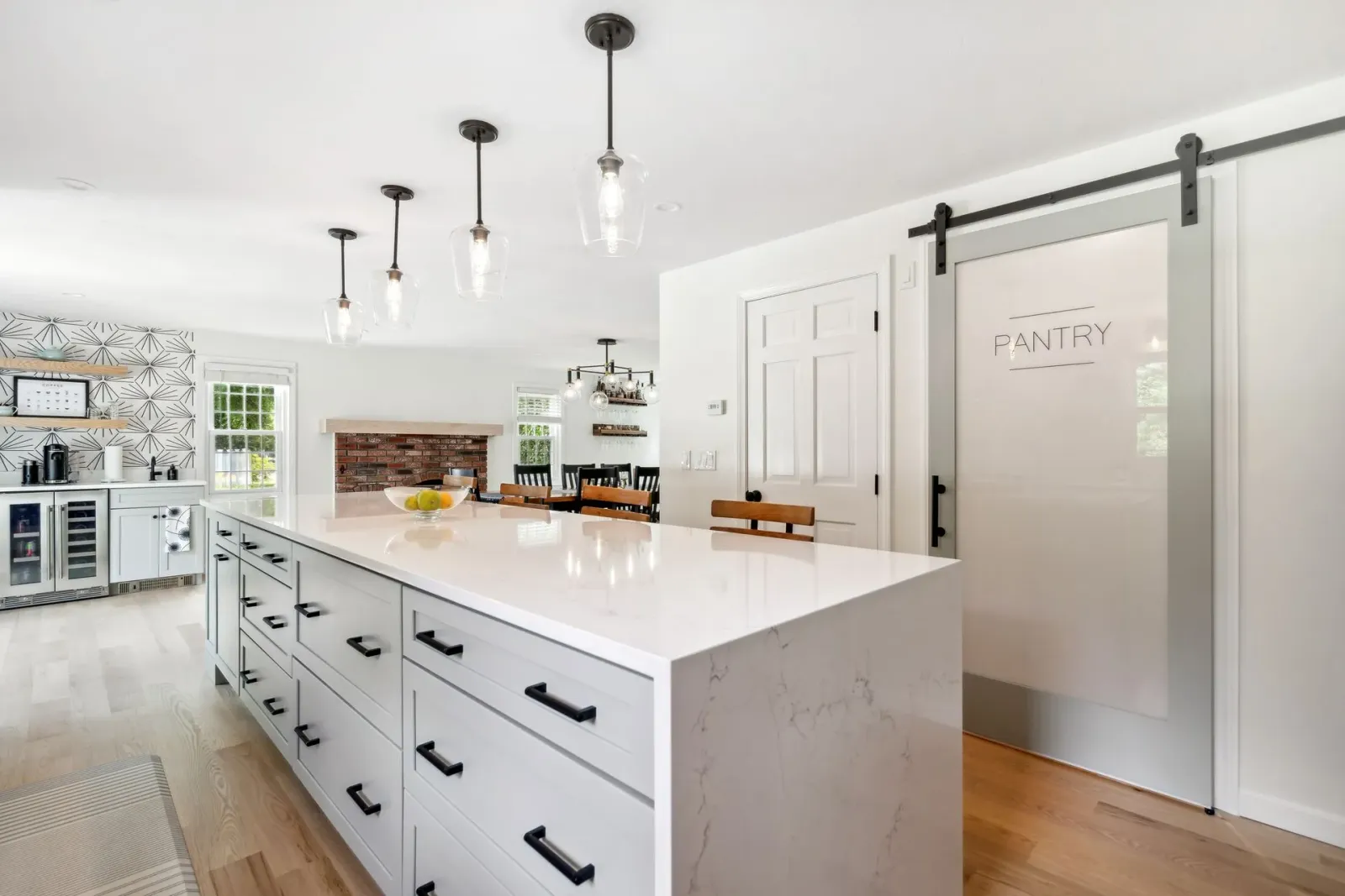 Bright, modern kitchen with large island, pantry door, pendant lights, and wooden floors.