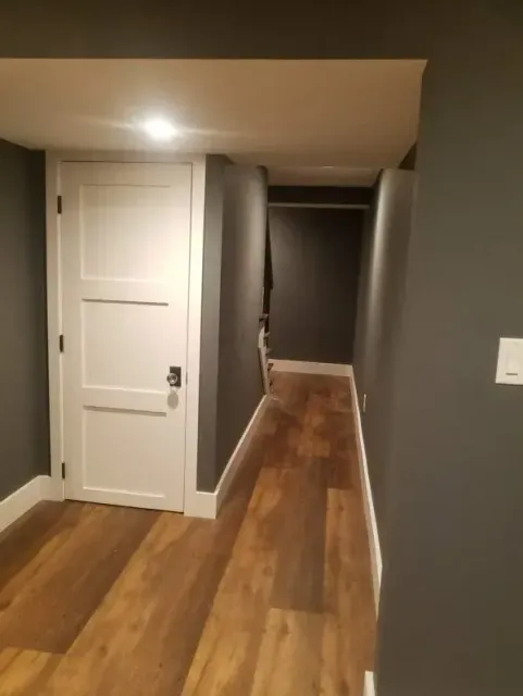 A narrow hallway with dark gray walls, a white door, and wood flooring.