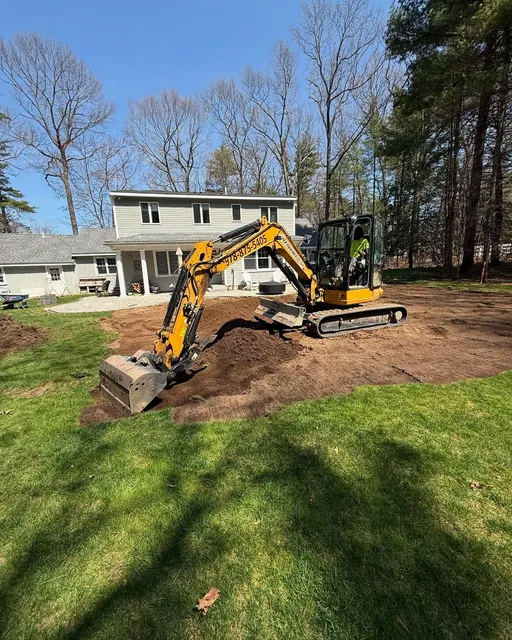 Yellow excavator digging in a backyard near a house on a sunny day.