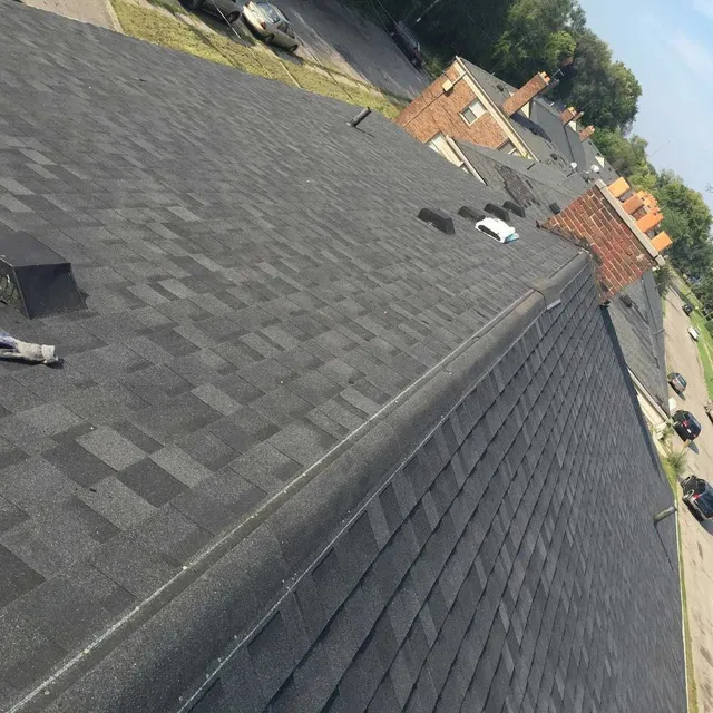 A high-angle view looking down the sloped surface of a dark gray shingled roof towards a parking lot below.