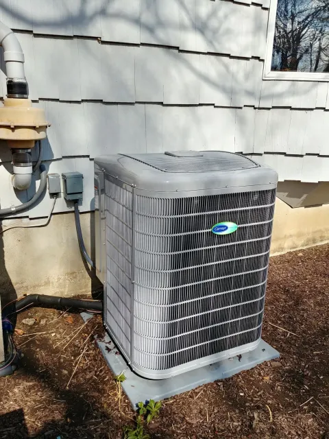 An air conditioner is sitting outside of a house next to a window.