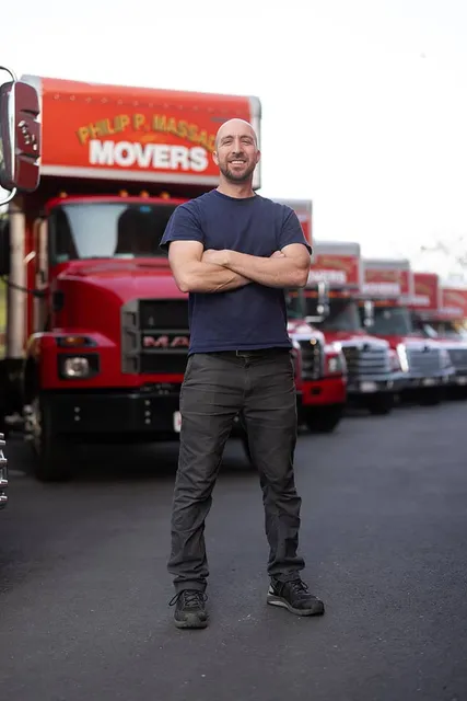 Man with arms crossed in front of red Massad Movers trucks