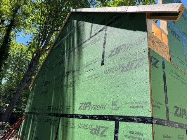 House under construction wrapped in green ZIP System sheathing in a wooded area