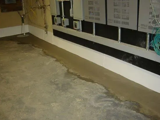Concrete basement floor with a long drain along the wall and exposed utility panels.