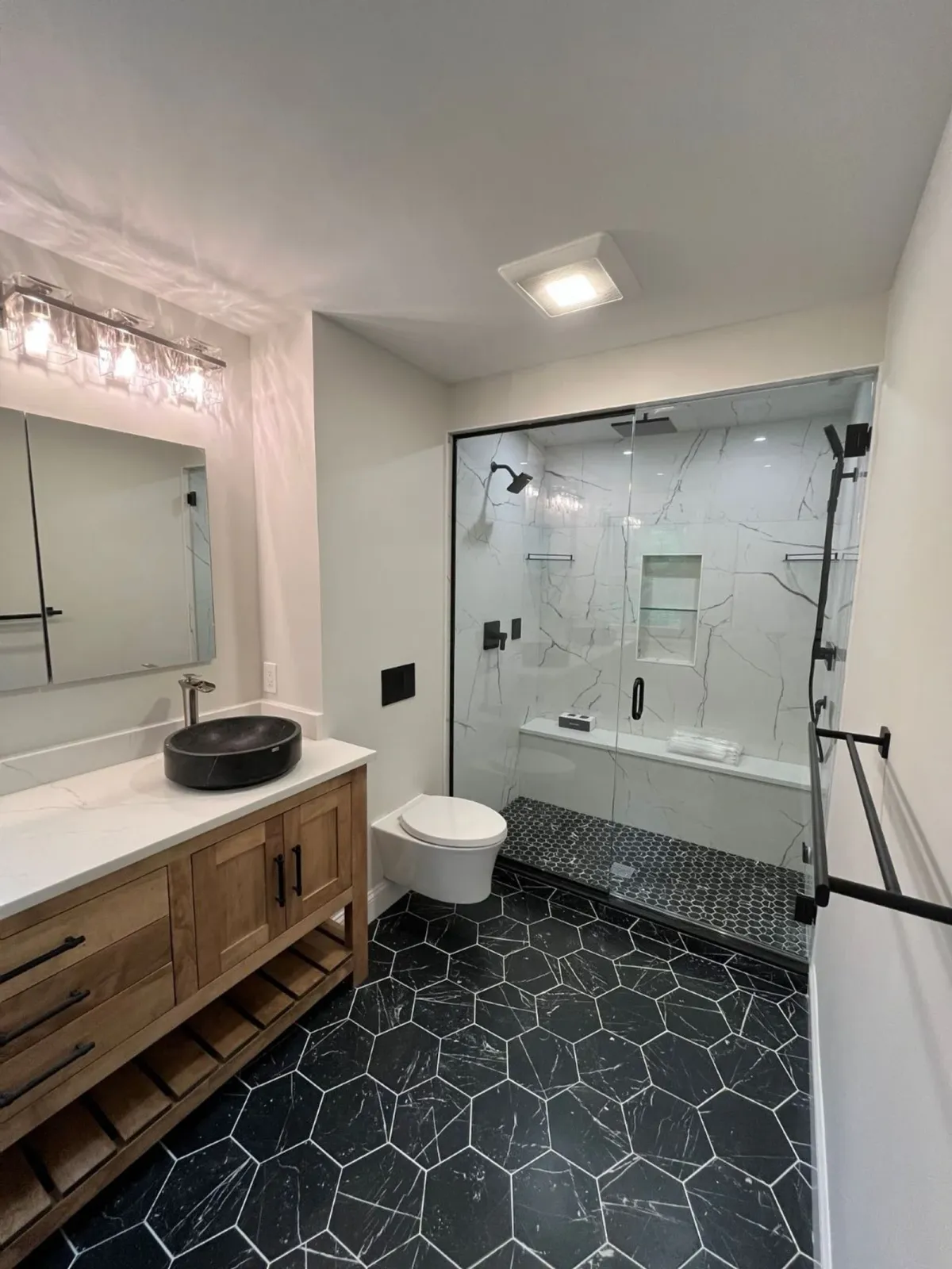a remodeled bathroom that has gorgeous recessed lighting installed in the shower and a newly installed bathroom ventilation