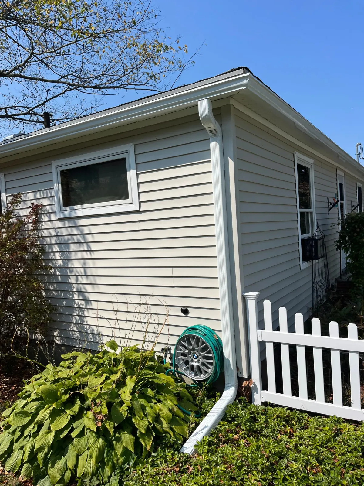 White house exterior with green shutters, downspout, and a white picket fence in a sunny yard