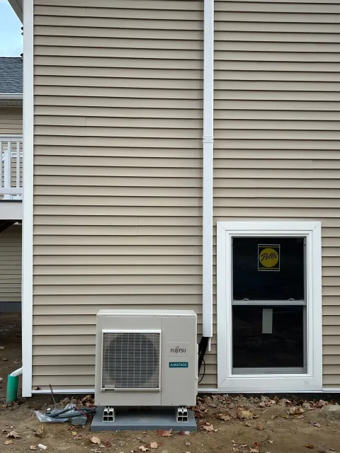 An air conditioner is installed on the side of a house next to a window.
