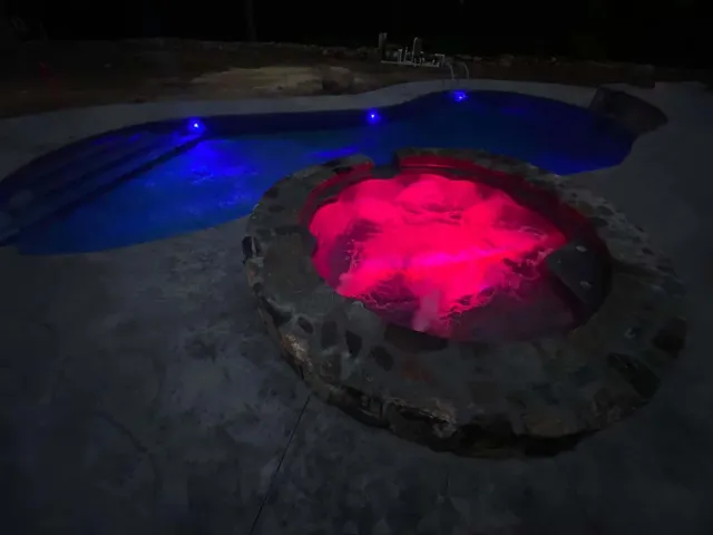 A hot tub is lit up at night next to a pool.