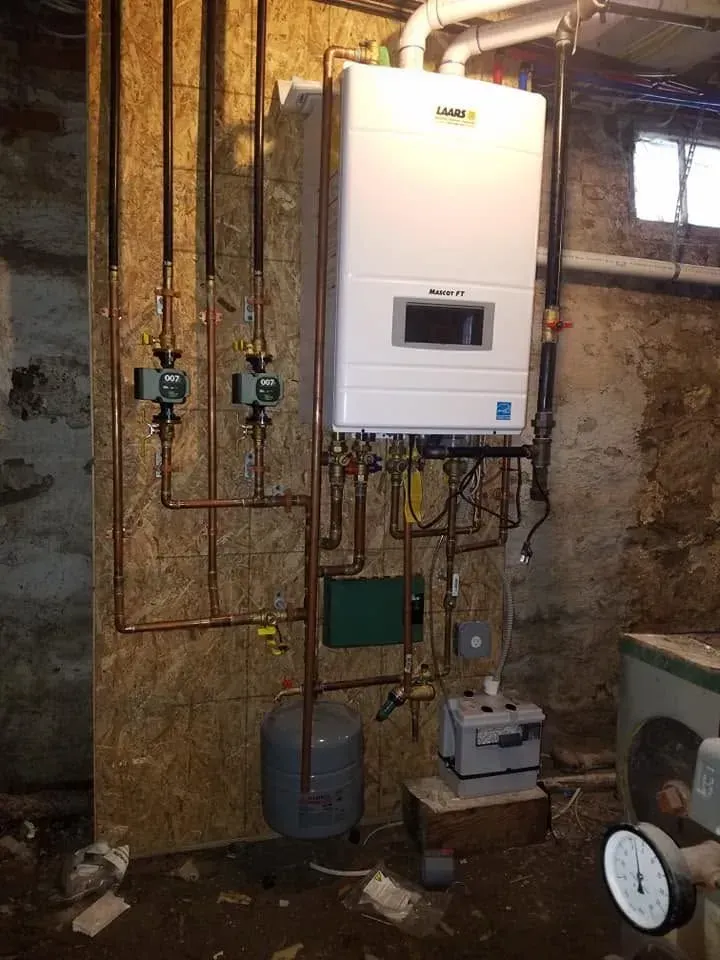 Wall-mounted boiler and copper pipes in an unfinished utility room with exposed insulation and a pressure gauge.