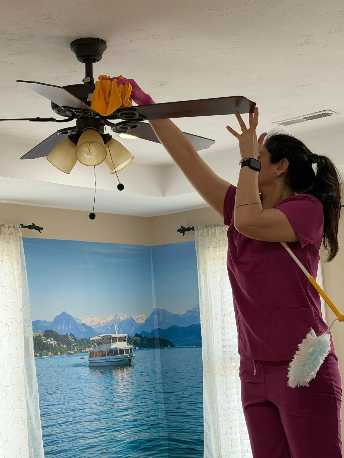 A RosyGloves cleaner carefully dusting a ceiling fan during a deep clean