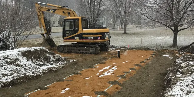 A yellow and black excavator on dirt road near trees.