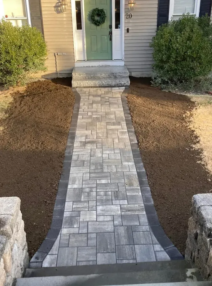 Stone pathway leading to a green door. Dark borders, mulch, and greenery on either side.
