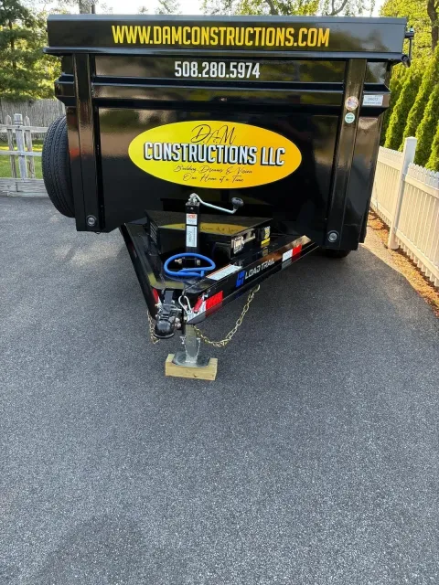 Black trailer with yellow “Construction LLC” logo and website parked on asphalt driveway.