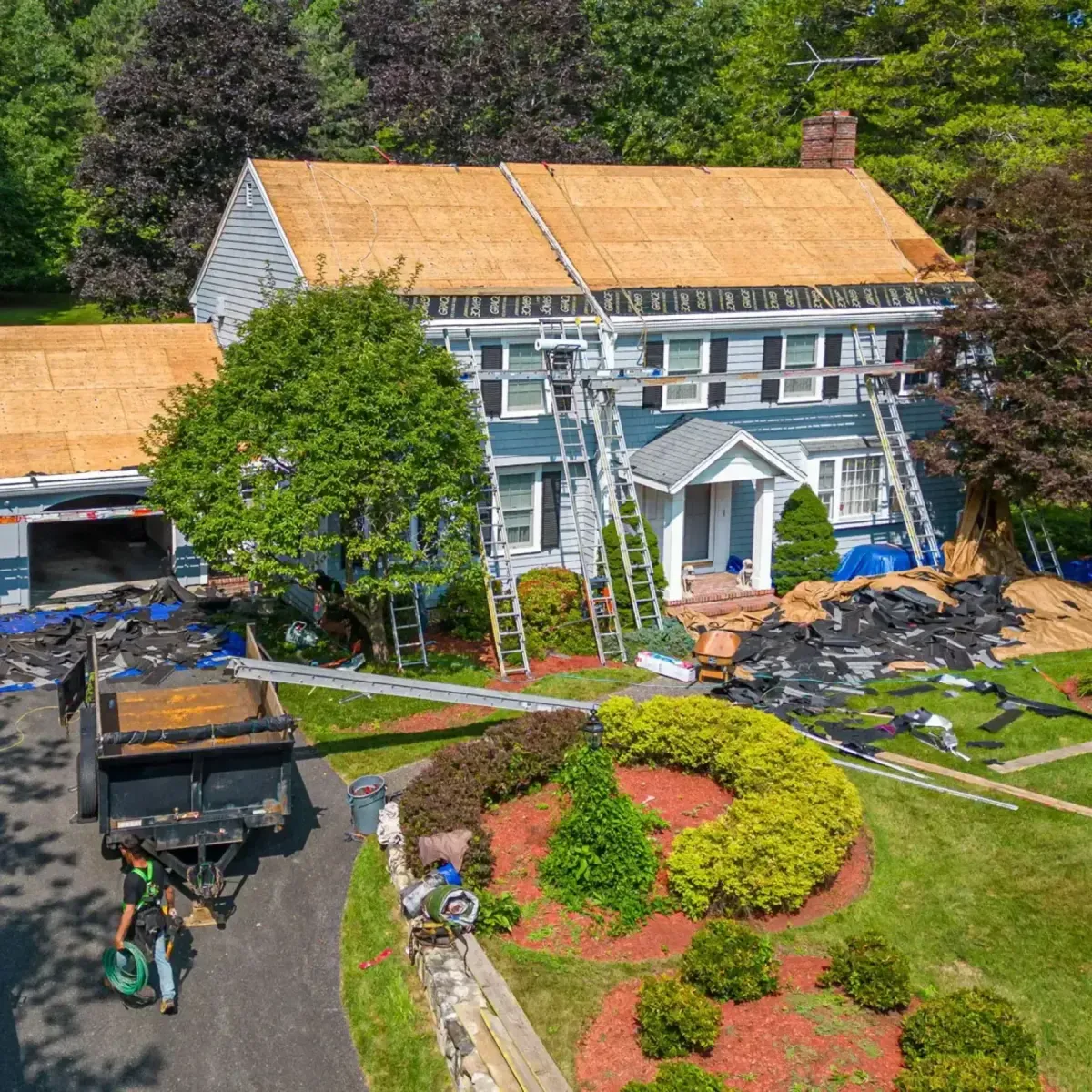 Roofing project in progress on a residential home with ladders, roofing materials, and landscaping, showcasing Crown Roofing's expertise in roof replacements.