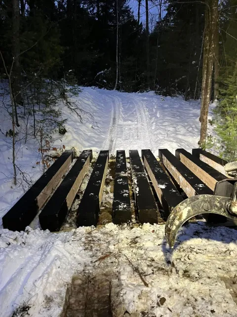 Black timber beams on snowy ground, forest background, tracks in snow.