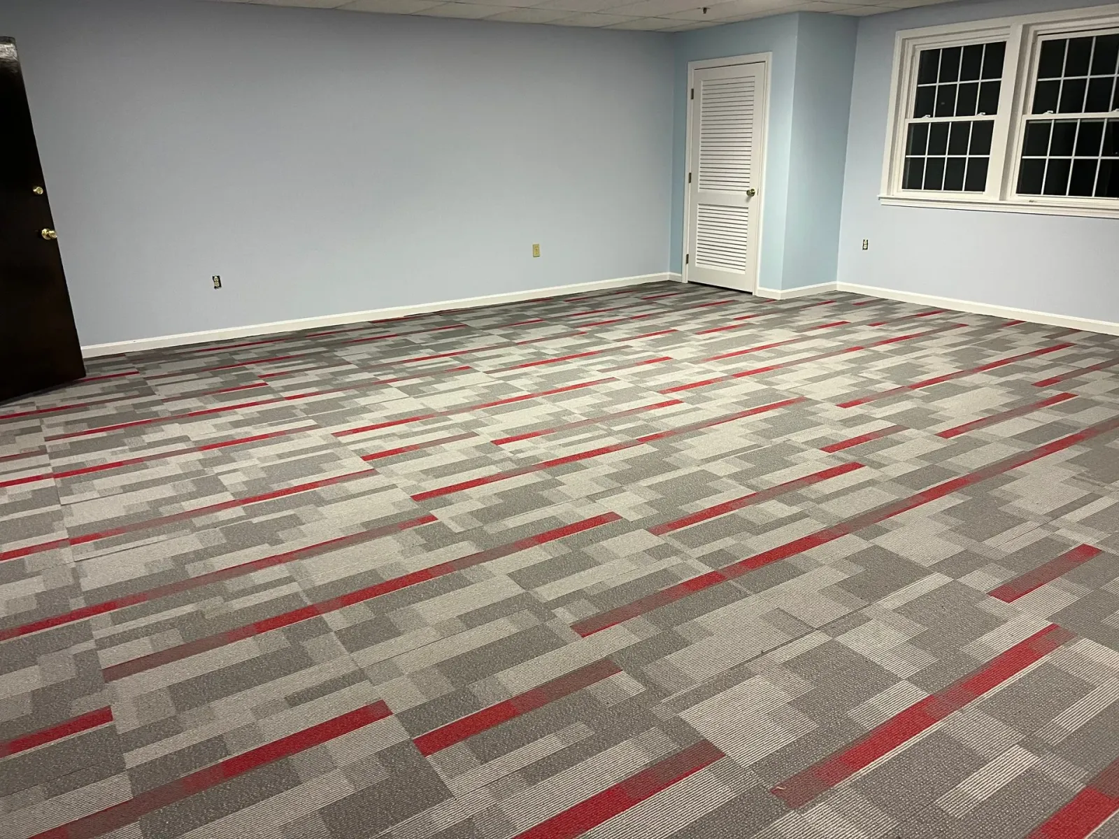 A large room with a carpeted floor and two windows.