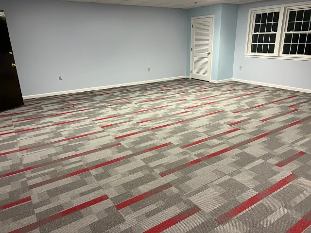 A large room with a carpeted floor and two windows.