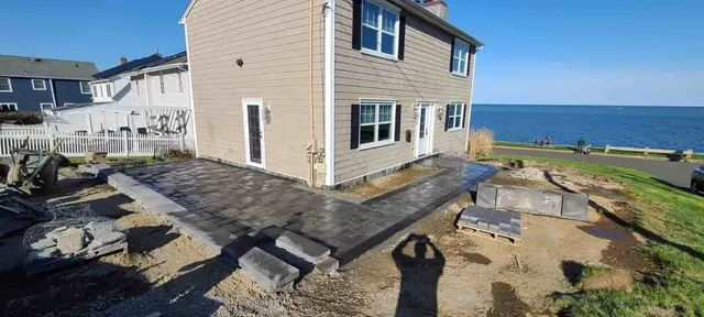 Coastal stone house with paved patio and benches overlooking the ocean on a sunny day