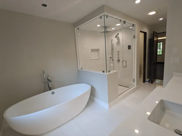 Modern bathroom with white freestanding bathtub, walk-in glass shower with white subway tiles, built-in shower niche, and gray walls.