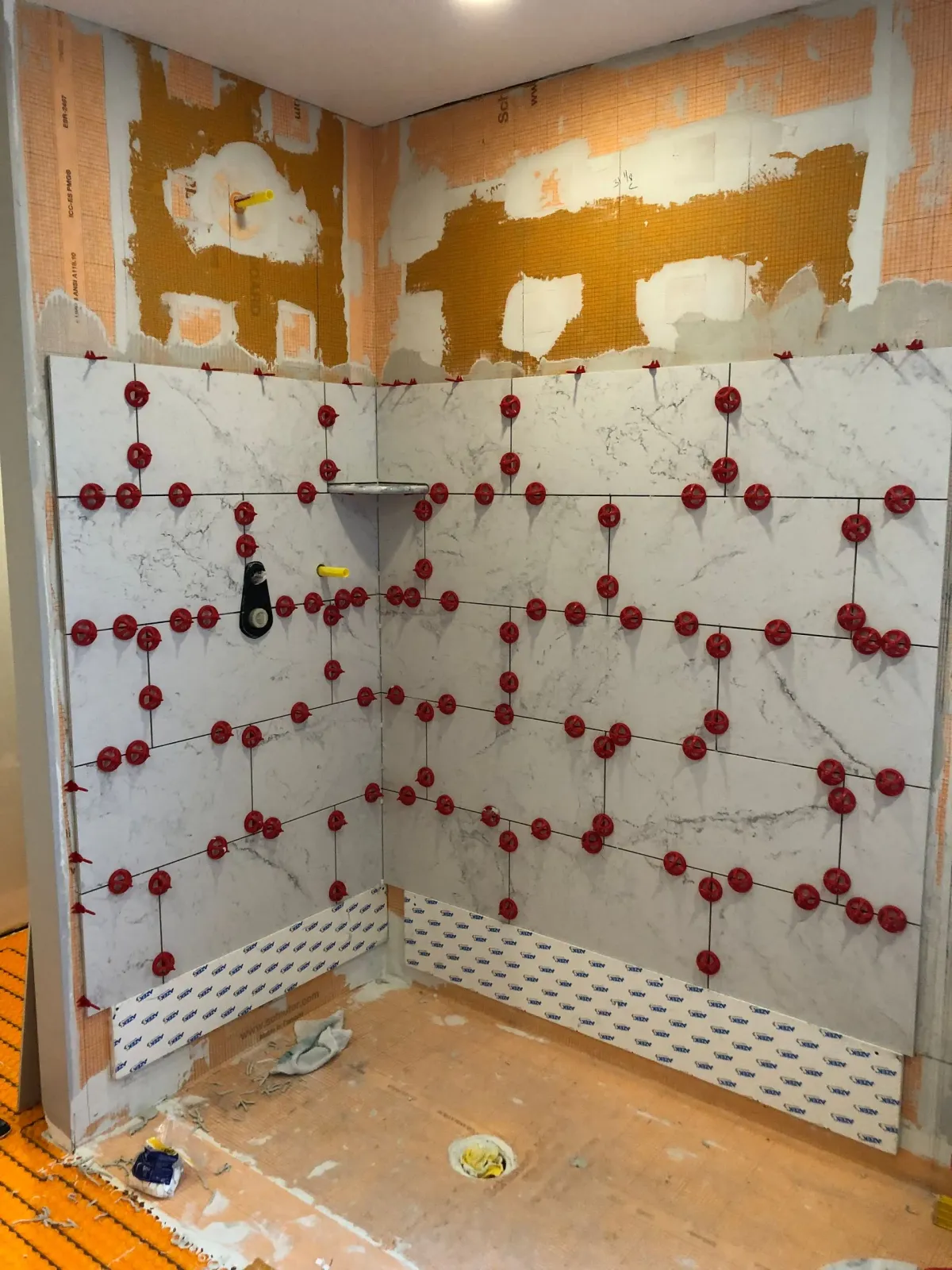 Partially tiled shower walls with red tile spacers and exposed drywall above