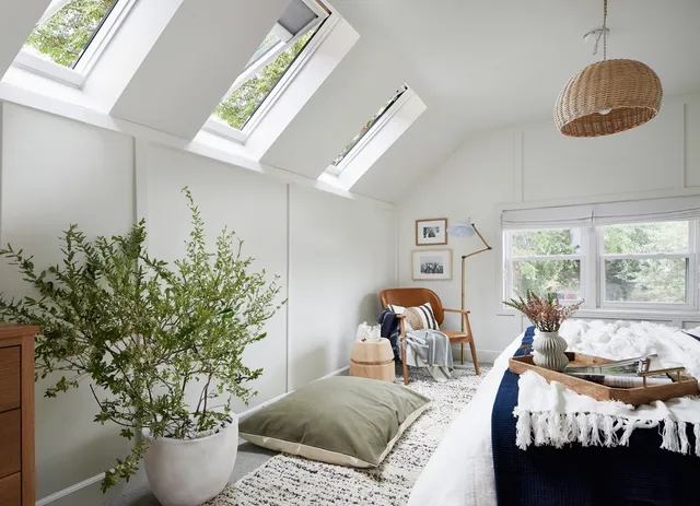 Bright attic bedroom with skylights, plants, and a bed by a window.