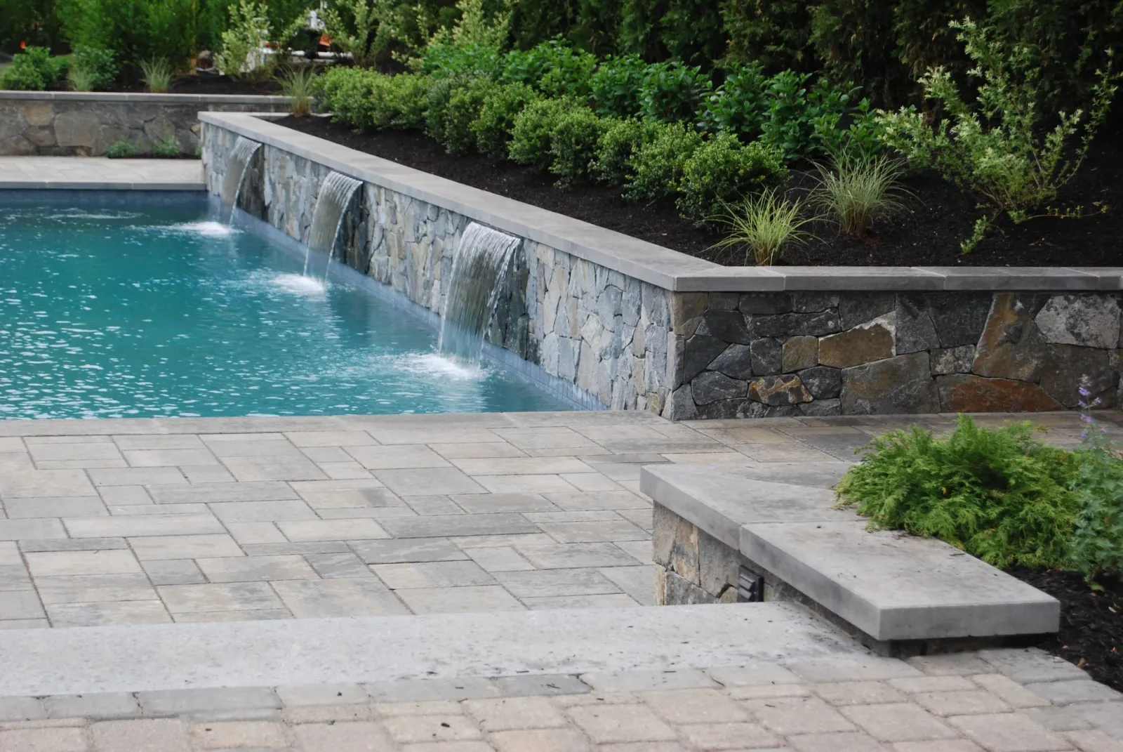 Sheer descent fountains at our pool project in Andover, MA create interest and soothing sound. A total backyard landscape transformation.