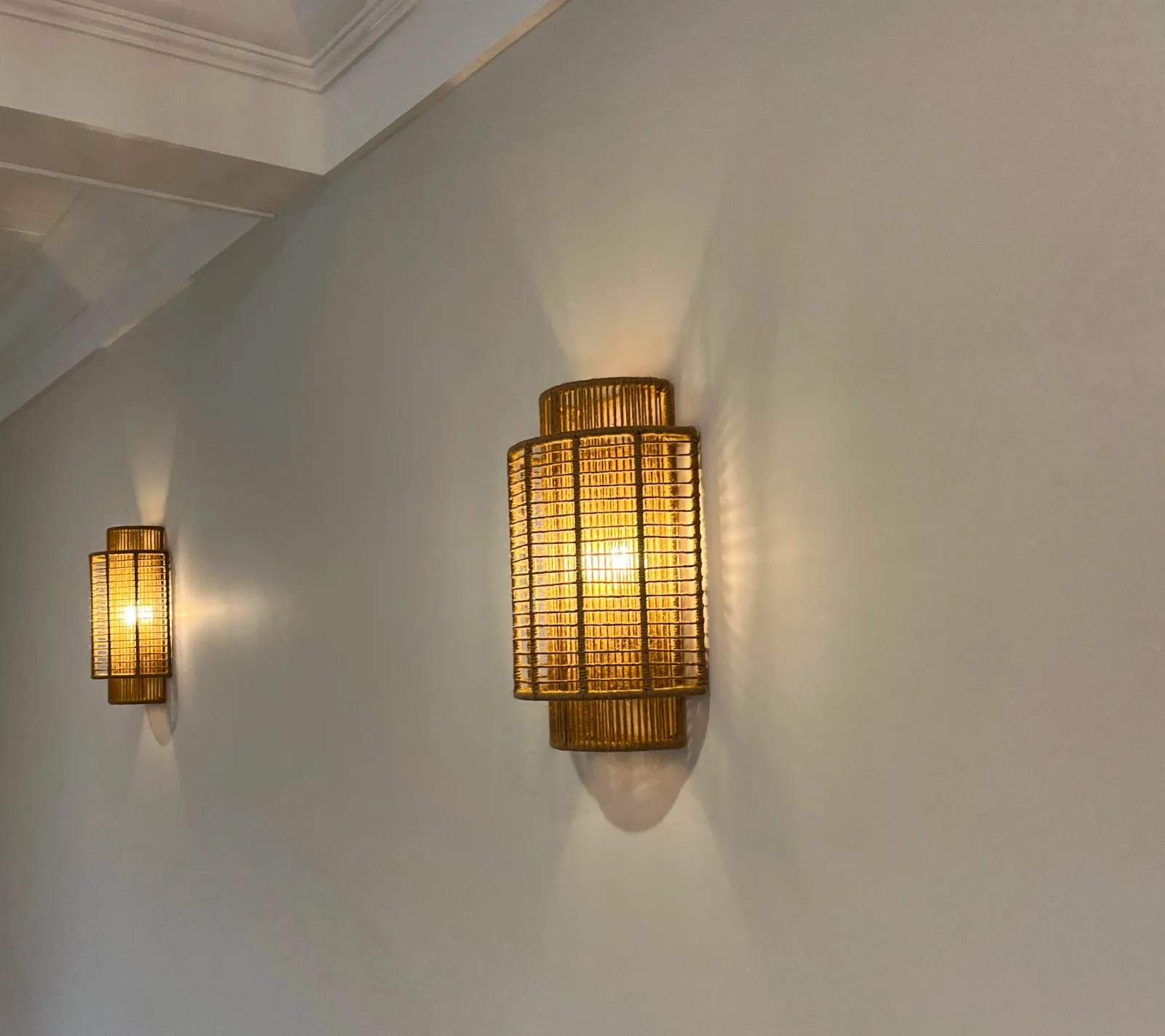 Two wall-mounted wicker lamps emitting warm light on a white wall.