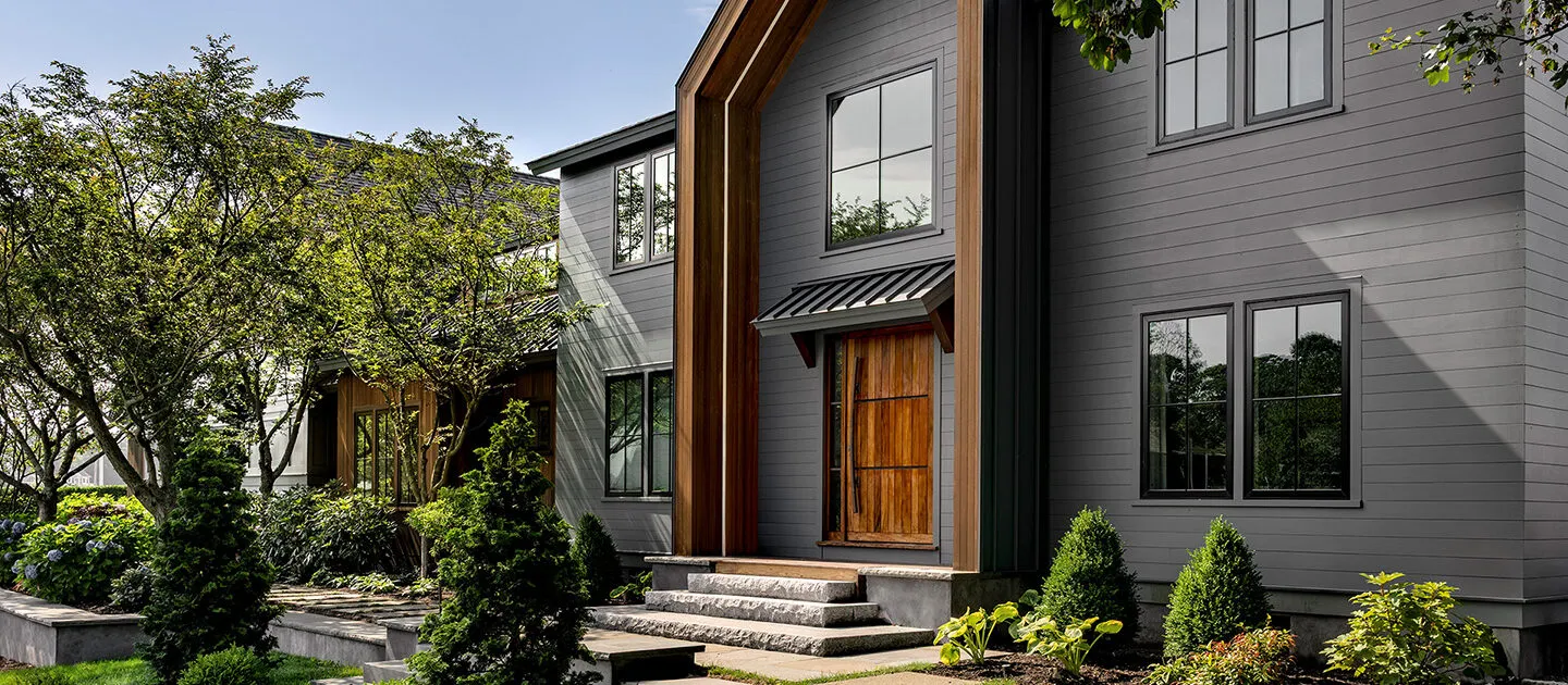 Modern custom outdoor living space with grey siding and wood accents.
