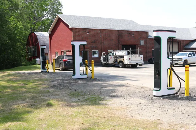 Electric vehicle charging station in front of a red brick building with trees in the background.