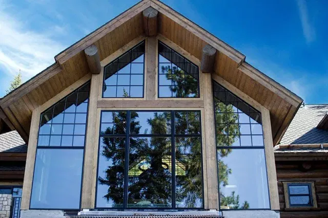 Modern cabin front with large triangular windows and blue sky reflecting in the glass