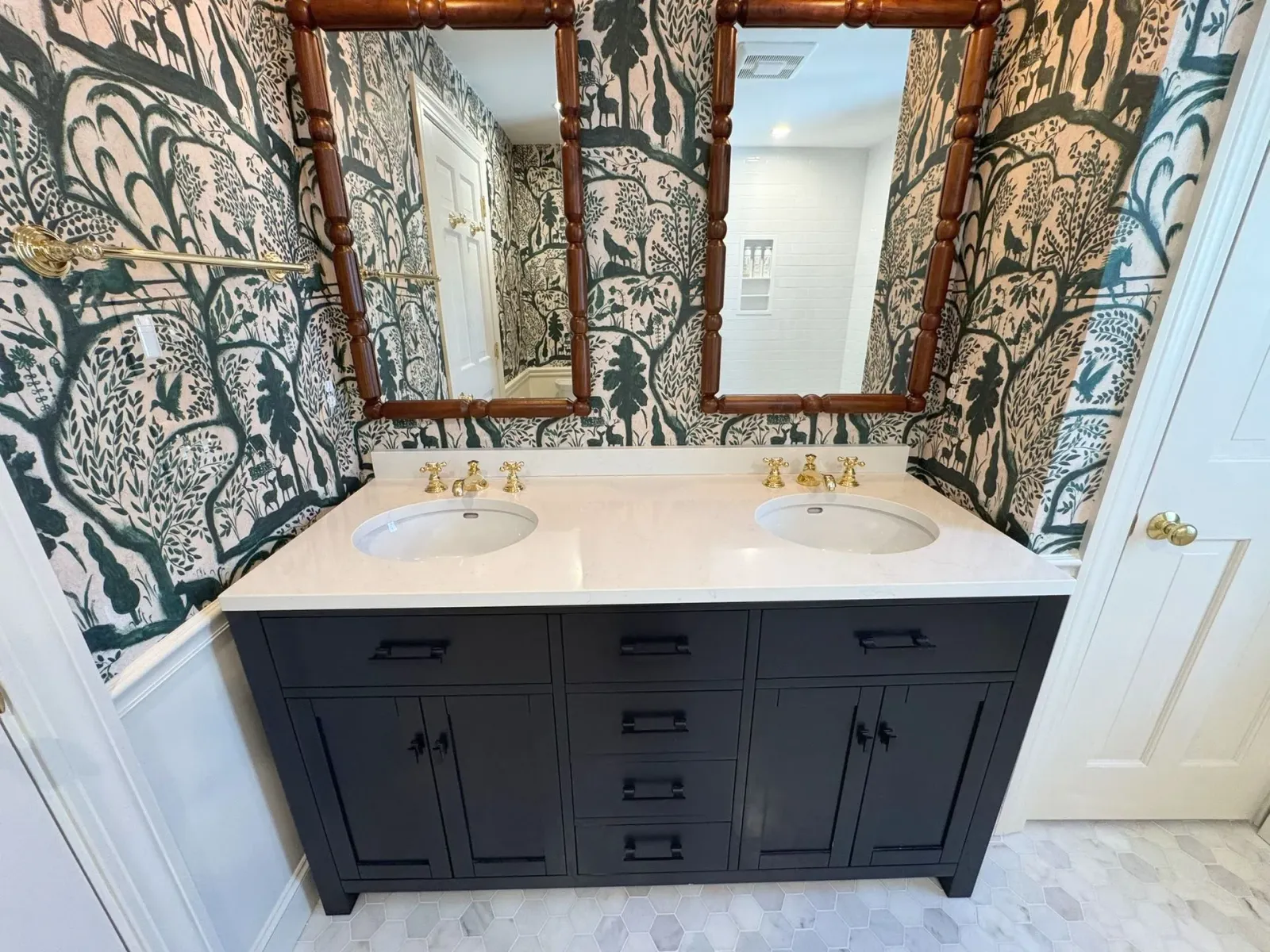 Double vanity bathroom sink with dark cabinets, white countertop, and patterned wallpaper with mirrors