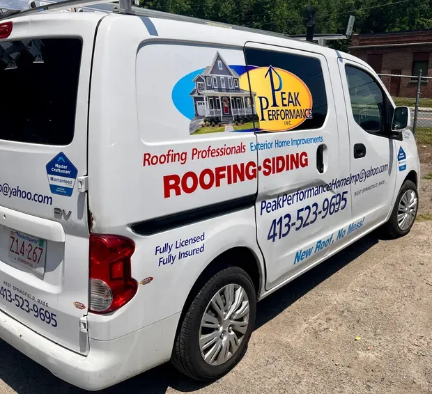White roofing and siding van with company logos and phone number parked outdoors at a job site