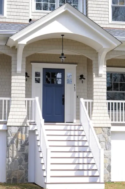 A white house with a covered porch, white railings, and a bold blue front door with a small window.