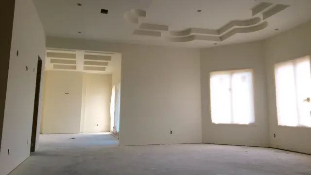 An open interior skim-coated throughout to a smooth uniform finish, with a stepped tray ceiling and plastic-masked windows
