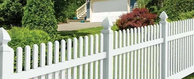 White picket fence in front of a house, surrounded by greenery.