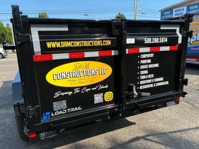 Black construction trailer with yellow and white company lettering and contact info on the side outdoors